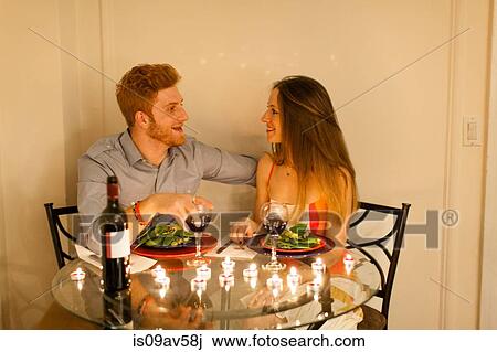 Stock Image - Couple at table face to face enjoying candlelit meal, smiling. Fotosearch