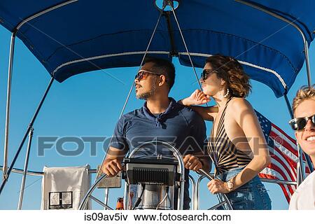 Stock Photo - Couple behind wheel of sailboat, enjoying view with friend. Fotosearch