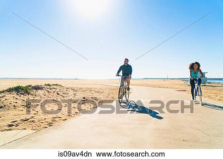 Couple cycling along pathway at beach View Large Photo Image Picture - Couple cycling along pathway at beach. Fotosearch