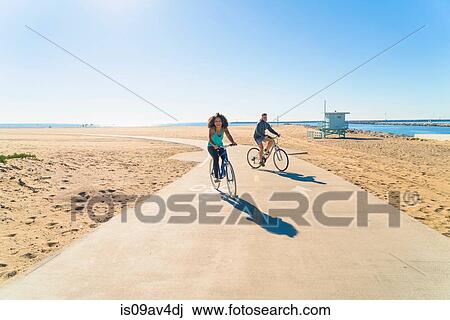 Couple cycling along pathway at beach View Large Photo Image Stock Image - Couple cycling along pathway at beach. Fotosearch
