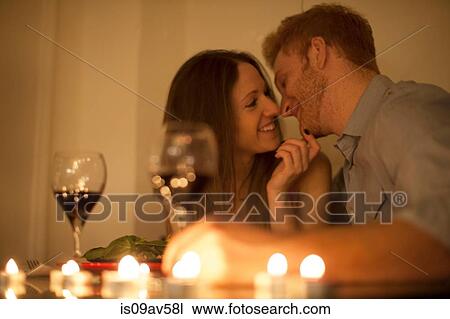 Stock Image - Couple enjoying a glass of red wine by candlelight, face to face smiling. Fotosearch