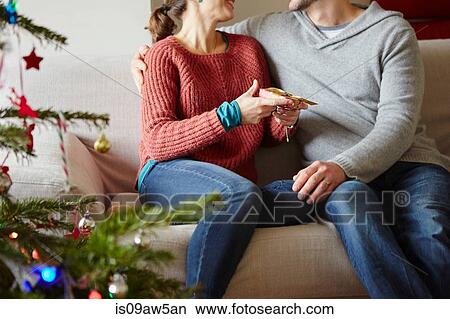 Couple handing xmas gifts on living room sofa View Large Photo Image Picture - Couple handing xmas gifts on living room sofa. Fotosearch
