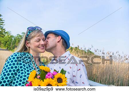 Couple holding flowers, kissing on cheek View Large Photo Image Stock Photo - Couple holding flowers, kissing on cheek. Fotosearch