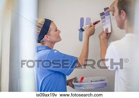 Stock Photo - Couple holding paint swatches comparing with paint on wall. Fotosearch