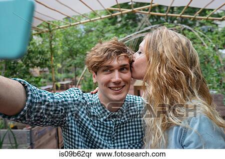 Stock Photography - Couple in garden kissing, taking selfie. Fotosearch