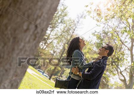Stock Image - Couple in park face to face hugging and smiling. Fotosearch