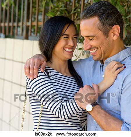 Stock Image - Couple in street hugging, smiling. Fotosearch