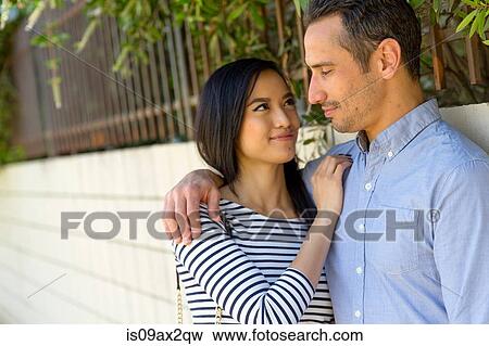 Stock Photo - Couple in street leaning against wall smiling. Fotosearch
