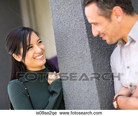 Stock Image - Couple leaning against column face to face smiling. Fotosearch