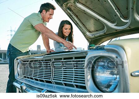 Stock Image - Couple looking at car engine smiling, Los Angeles, California, USA. Fotosearch