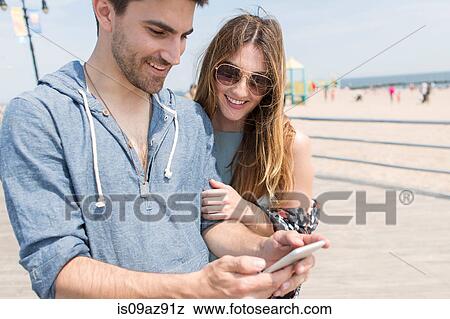 Couple looking at smartphone smiling, Coney island, Brooklyn, New York, USA View Large Photo Image Stock Photo - Couple looking at smartphone smiling, Coney island, Brooklyn, New York, USA. Fotosearch