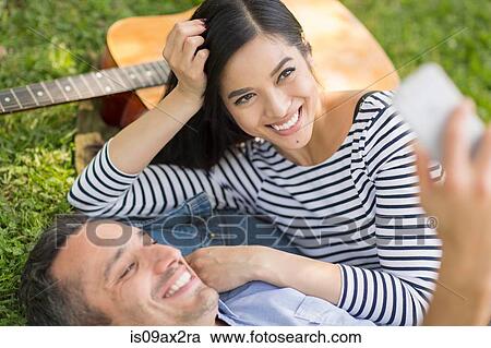 Couple lying on grass using smartphone to take selfie View Large Photo Image Stock Image - Couple lying on grass using smartphone to take selfie. Fotosearch