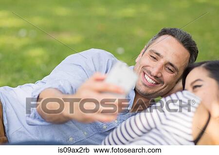 Couple lying on grass using smartphone to take selfie View Large Photo Image Stock Image - Couple lying on grass using smartphone to take selfie. Fotosearch
