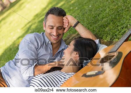 Couple lying on grass with acoustic guitar smiling View Large Photo Image Picture - Couple lying on grass with acoustic guitar smiling. Fotosearch