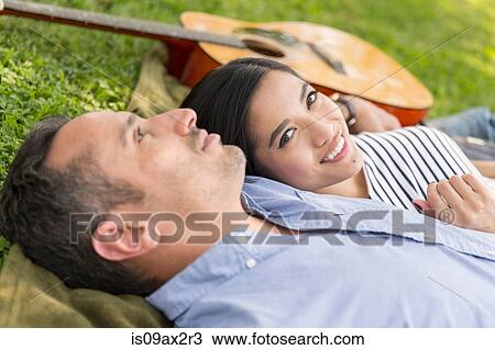 Couple lying on grass with acoustic guitar looking at camera smiling View Large Photo Image Stock Image - Couple lying on grass with acoustic guitar looking at camera smiling. Fotosearch
