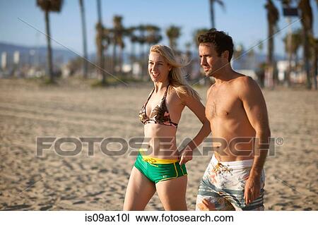Stock Image - Couple on beach wearing shorts. Fotosearch