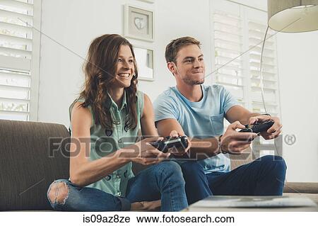 Couple on sofa using video game controller smiling View Large Photo Image Stock Image - Couple on sofa using video game controller smiling. Fotosearch