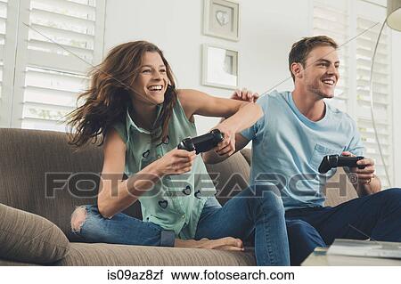 Stock Image - Couple on sofa using video game controller smiling. Fotosearch