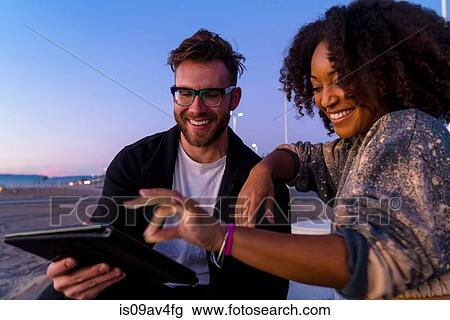 Couple outdoors, beside beach, looking at digital tablet View Large Photo Image Stock Image - Couple outdoors, beside beach, looking at digital tablet. Fotosearch