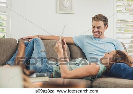 Couple relaxing on sofa using digital tablet smiling View Large Photo Image Stock Image - Couple relaxing on sofa using digital tablet smiling. Fotosearch