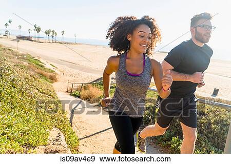Stock Photo - Couple running along pathway by beach. Fotosearch