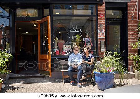 Couple sitting on bench, outside bakery, holding coffee cups View Large Photo Image Stock Photo - Couple sitting on bench, outside bakery, holding coffee cups. Fotosearch