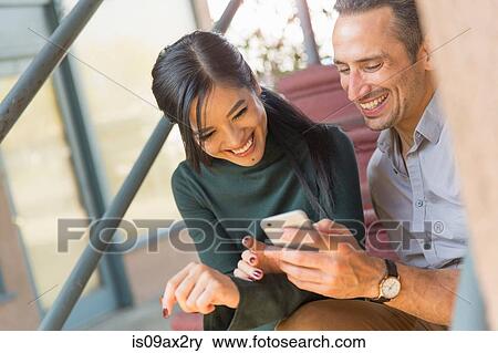 Couple sitting on stairway using smartphone smiling View Large Photo Image Stock Photo - Couple sitting on stairway using smartphone smiling. Fotosearch
