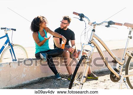 Stock Photo - Couple sitting on wall, taking a break, bicycles beside them. Fotosearch