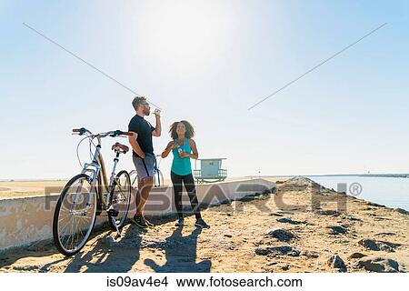 Couple taking a break from cycling, holding bottle drink View Large Photo Image Picture - Couple taking a break from cycling, holding bottle drink. Fotosearch