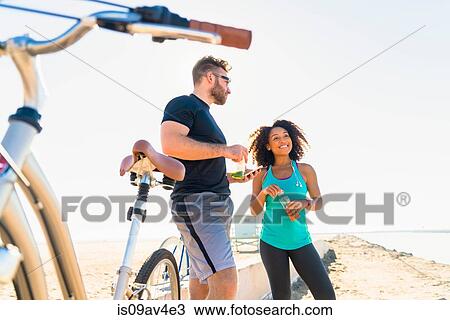 Stock Image - Couple taking a break from cycling, holding bottle drink. Fotosearch