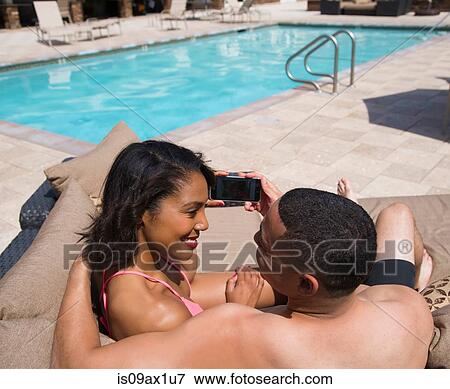 Stock Photo - Couple taking selfie on sofa beside pool. Fotosearch