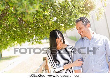 Couple underneath tree linking arms smiling View Large Photo Image Stock Photography - Couple underneath tree linking arms smiling. Fotosearch