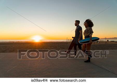 Couple walking along pathway by beach, holding skateboards View Large Photo Image Picture - Couple walking along pathway by beach, holding skateboards. Fotosearch