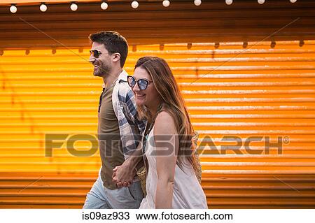 Couple walking by orange shutters holding hands smiling, Coney island, Brooklyn, New York, USA View Large Photo Image Stock Image - Couple walking by orange shutters holding hands smiling, Coney island, Brooklyn, New York, USA. Fotosearch