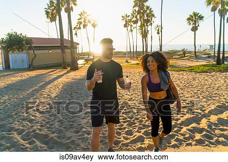 Couple wearing sports clothing, walking along beach, talking View Large Photo Image Stock Photo - Couple wearing sports clothing, walking along beach, talking. Fotosearch