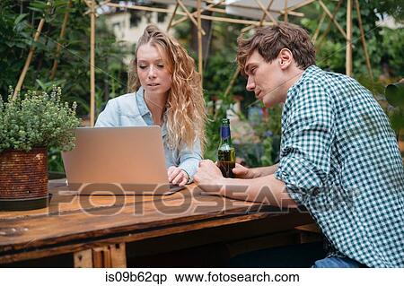 Stock Photography - Couple with beer in garden using laptop. Fotosearch