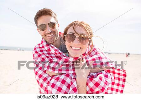 Couple wrapped in picnic blanket looking at camera smiling, Coney island, Brooklyn, New York, USA View Large Photo Image Stock Photo - Couple wrapped in picnic blanket looking at camera smiling, Coney island, Brooklyn, New York, USA. Fotosearch
