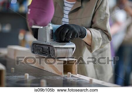 Stock Image - Cropped shot of female carpenter sanding wood in furniture making workshop. Fotosearch