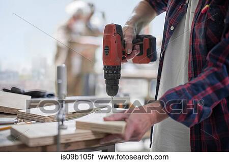 Stock Image - Cropped shot of female carpenter drilling wood in furniture making workshop. Fotosearch