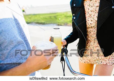 Stock Image - Cropped shot of young couple holding juice and coffee drinks at coast. Fotosearch