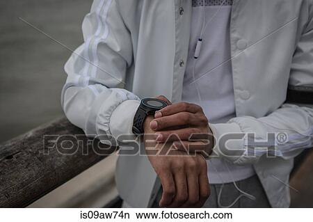 Picture - Cropped shot of young man training on riverside at dawn timing on smartwatch. Fotosearch