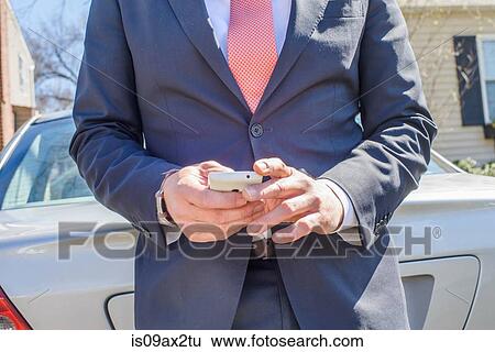 Cropped view of business man leaning against car using smartphone View Large Photo Image Stock Photograph - Cropped view of business man leaning against car using smartphone. Fotosearch