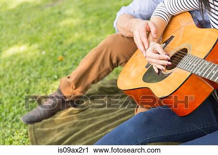 Cropped view of couple sitting on grass playing acoustic guitar View Large Photo Image Stock Image - Cropped view of couple sitting on grass playing acoustic guitar. Fotosearch