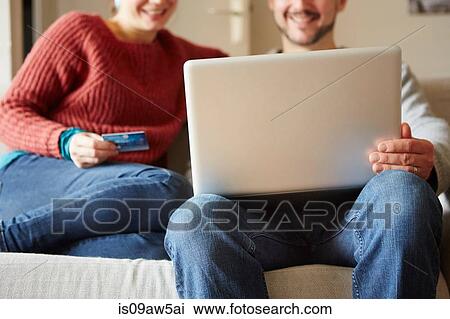 Stock Image - Cropped view of couple sitting on sofa using laptop and credit card. Fotosearch