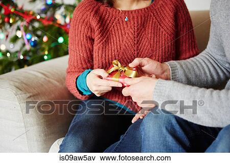 Cropped view of couples hands handing xmas gift on living room sofa View Large Photo Image Stock Photo - Cropped view of couples hands handing xmas gift on living room sofa. Fotosearch