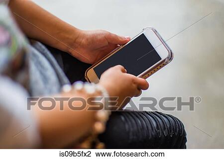 Stock Image - Cropped view of girl holding smartphone. Fotosearch
