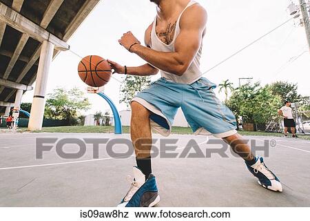 Stock Photo - Cropped view of man on basketball court running, bouncing basketball. Fotosearch
