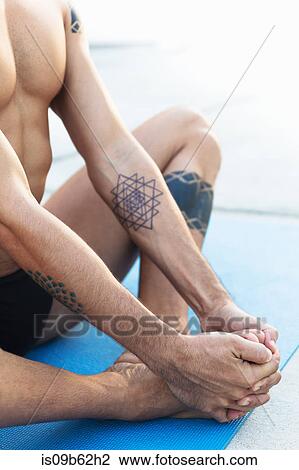 Stock Image - Cropped view of man practicing yoga, sitting in lotus position on yoga mat. Fotosearch