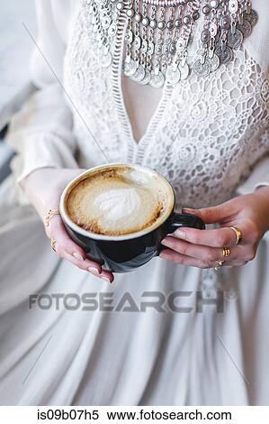 Stock Photography - Cropped view of woman wearing white dress holding coffee cup. Fotosearch