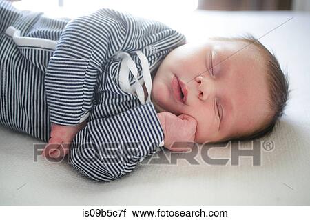 Stock Image - Cute baby boy with hand on chin asleep on bed. Fotosearch
